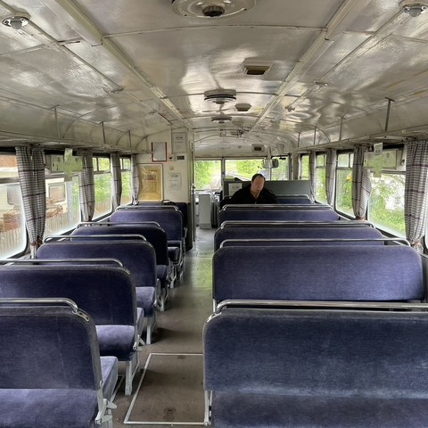 Blick in den Innenraum des Schienenbusses mit blauen Sitzbänken und Gardinen an den Fenstern.