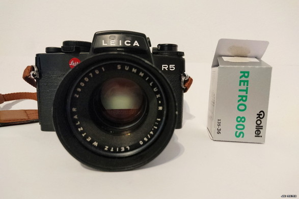 Farbfoto einer Leica R5 mit einem 50 mm-Objektiv (Leitz Summilux), Baujahr ca. 1986, mit der Schachtel eines Rollei Retro 80S-Schwarzweißfilms rechts daneben.