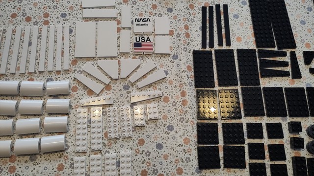 Klemmbausteine in weiss und schwarz ordentlich auf geblümter Tischdecke angeordnet, zwei Steine mit jeweils US-Flagge und dem Schriftzug NASA Atlantis